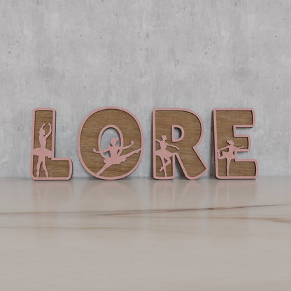 Vue de face des lettres en bois avec silhouettes de ballerines. Idéal pour une décoration artistique. | Vooraanzicht van houten naamletters met ballerina design, perfect voor decoratie.